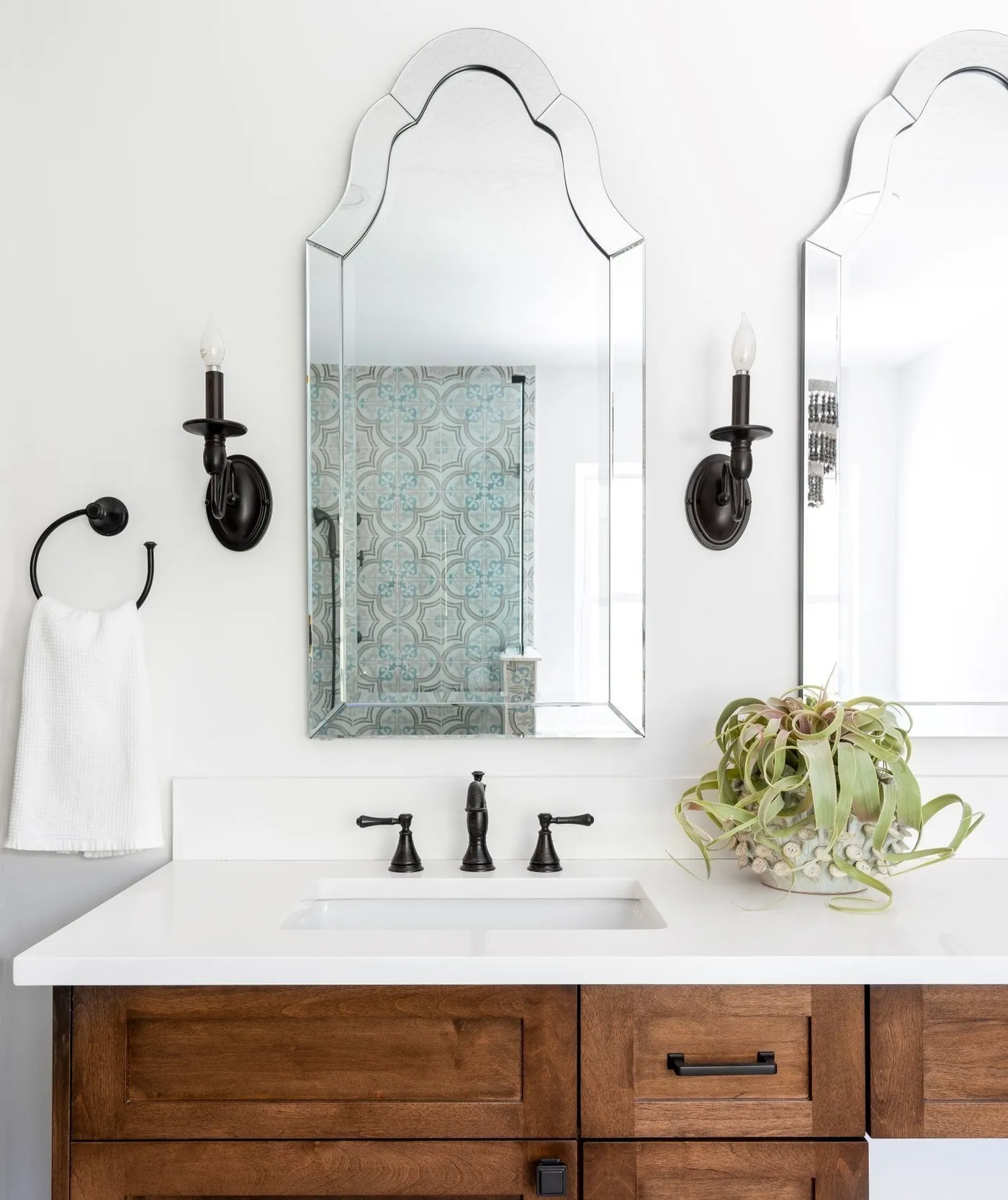 A white bathroom with a walnut vanity, matte black faucet and arched mirrors
