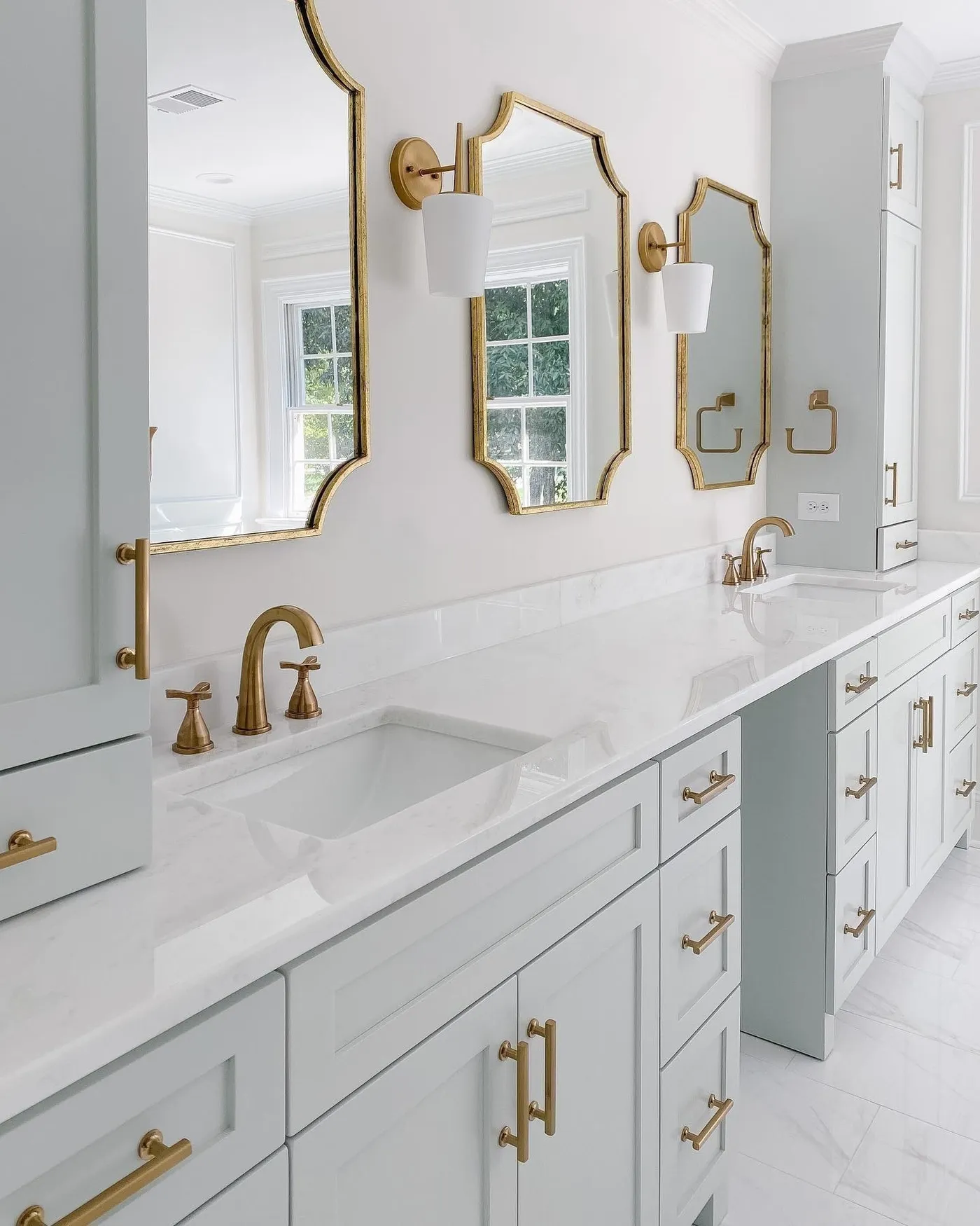 A white double vanity with gold faucets and arched mirrors