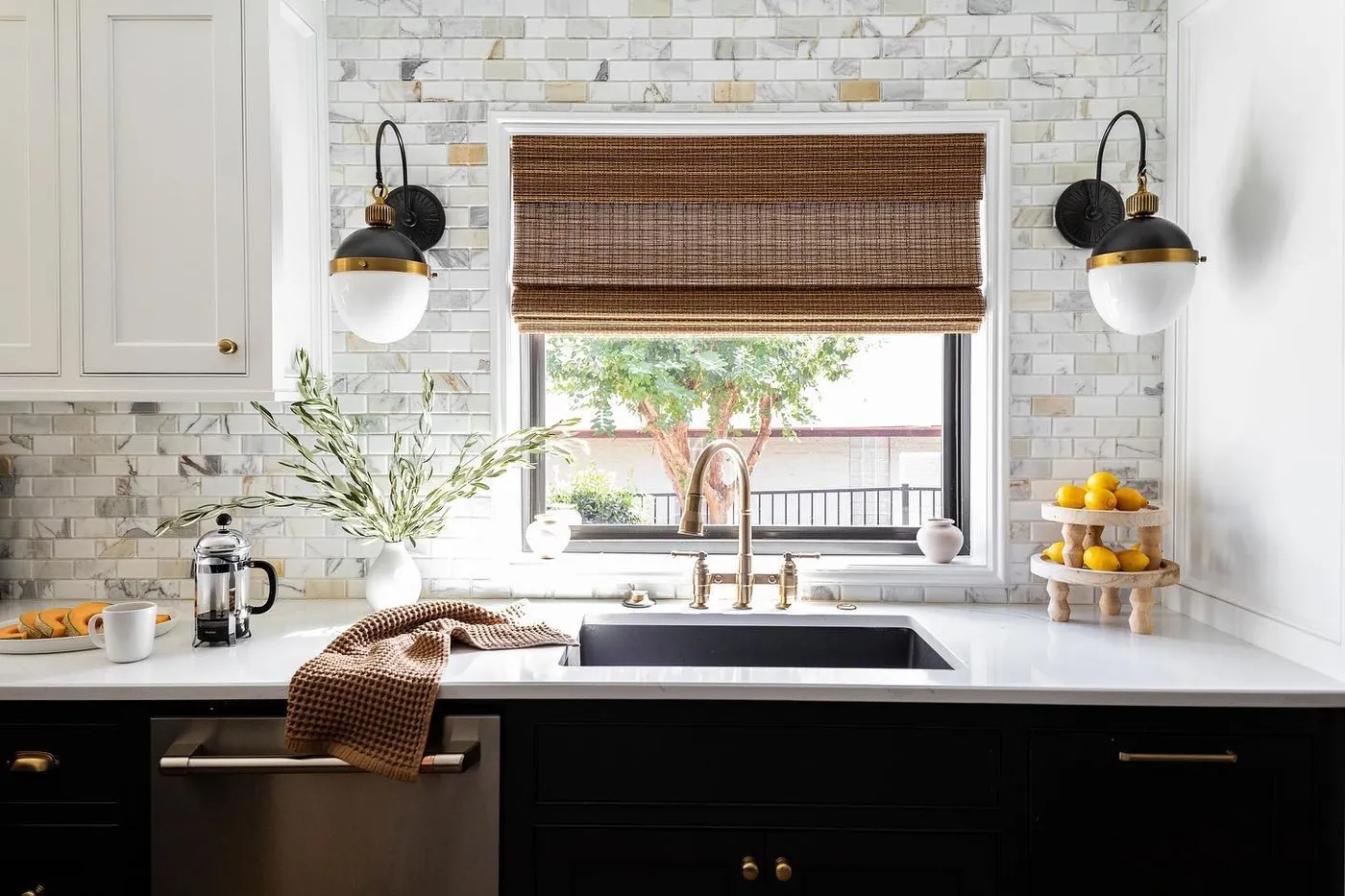 A brass bridge faucet over a white marble counter with black lower cabinets