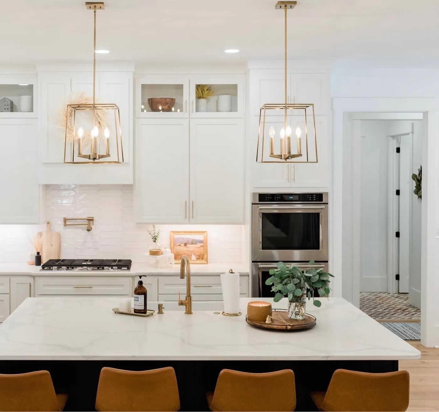 A white kitchen island with marble top, brass pendants and a gold faucet