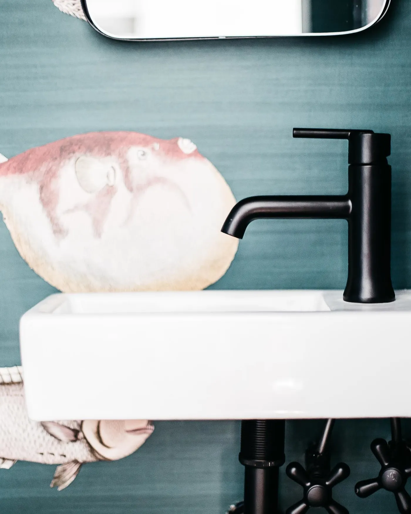 A matte black single-handle faucet over a white wall-hung basin on teal tile