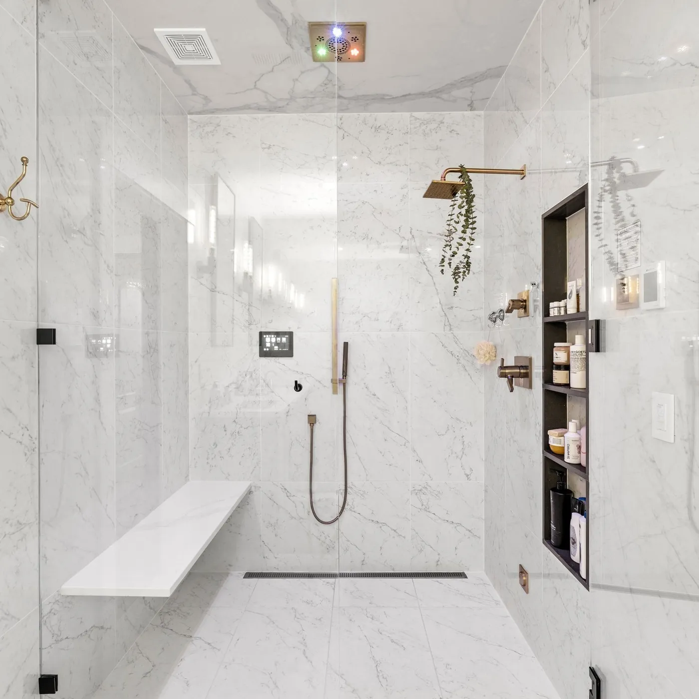 A marble walk-in shower with brushed bronze fittings and a bench